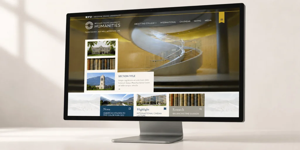 BYU College of Humanities homepage displayed on a slim desktop monitor against a warm neutral studio background.